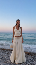 Front view of ivory halter ruched top and flowing maxi skirt set on a beach