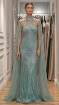 Front view of model wearing sage green embellished evening gown with cape