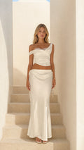 Front view of woman wearing white satin lace-trim crop top and midi skirt set on stairs