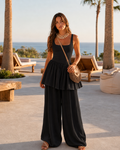 Woman wearing a black square neck sleeveless jumpsuit with tiered waist and wide leg pants