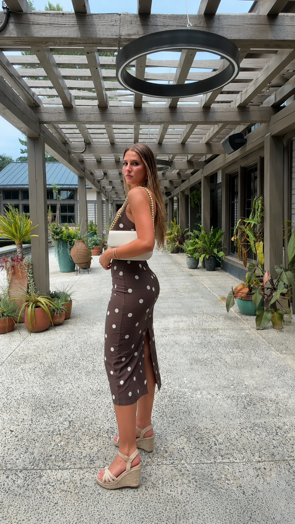 Side view of chocolate brown polka dot fitted midi dress with back slit