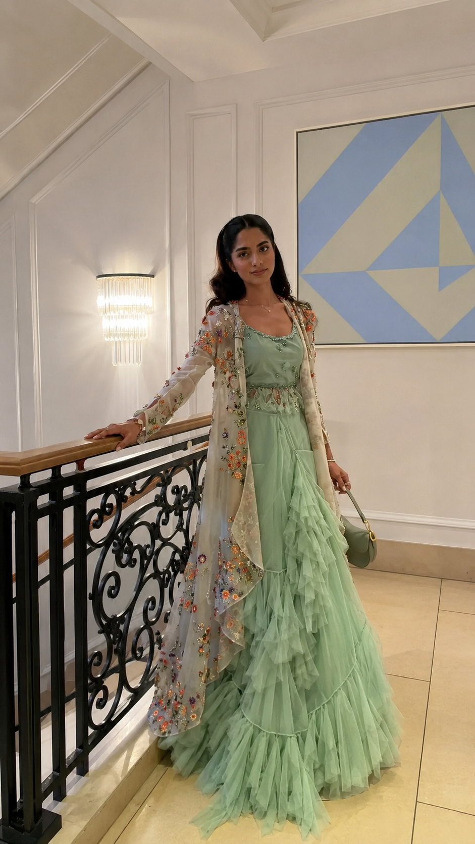 Woman wearing a mint green layered ruffle gown with a floral embroidered sheer cape