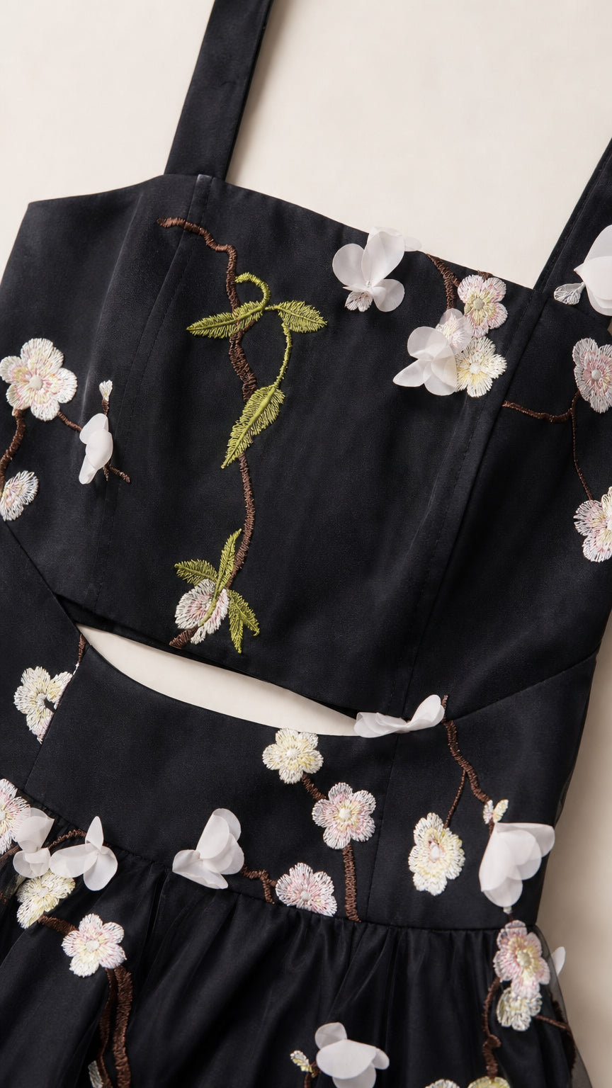 Close-up detail of bodice embroidery and waist cutout on black dress