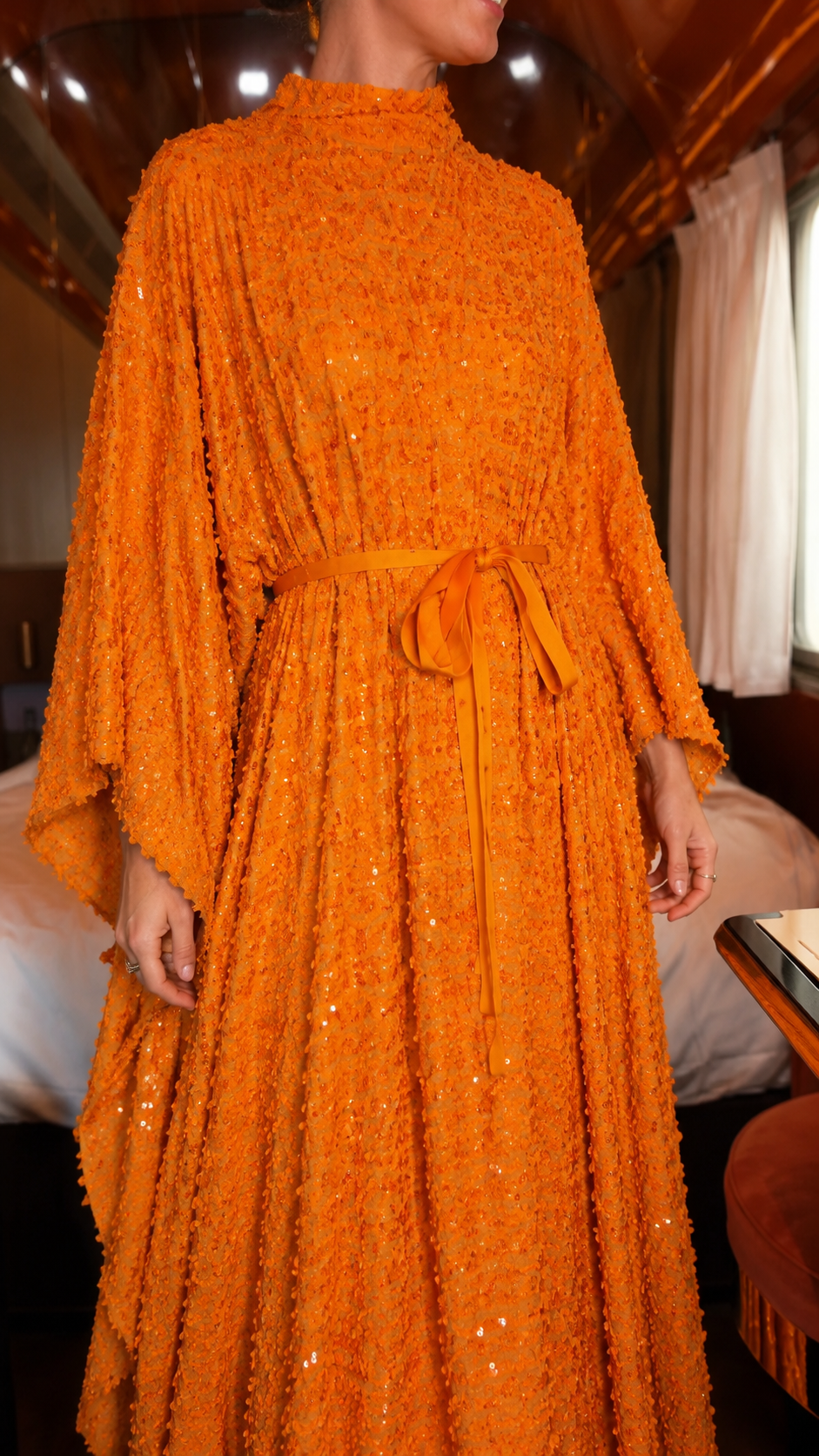 Close-up of orange textured shimmer maxi dress with self-tie belt and draped sleeve