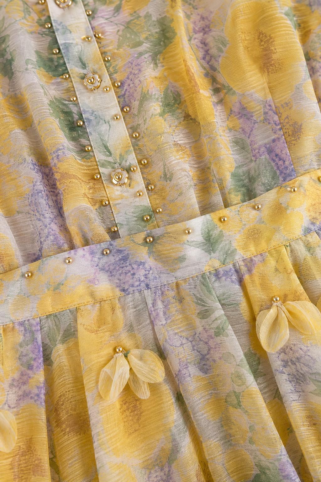 Close-up detail of fabric, buttons, and pleats on yellow floral dress
