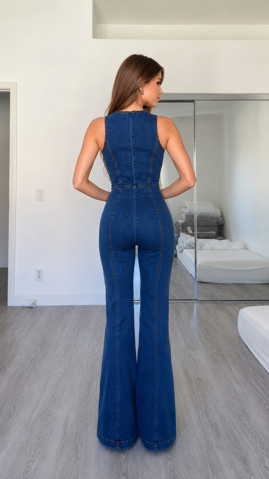 Back view of dark wash sleeveless denim jumpsuit with full-length flared leg