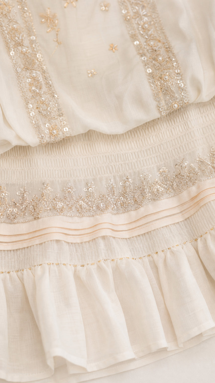 Close-up of metallic embroidery and ruffle hem details on white romper